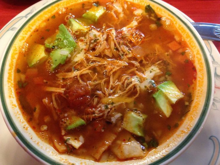 a bowl of soup with noodles, meat and avocado on the side sitting on a table