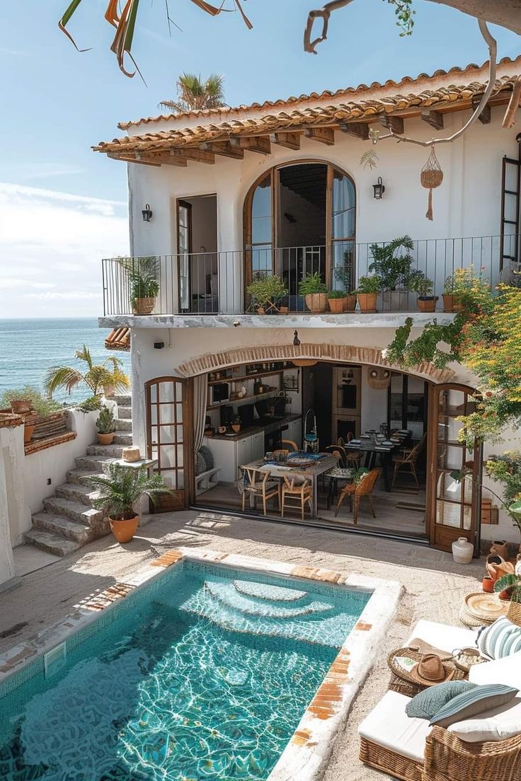 an outdoor swimming pool in front of a house next to the ocean with wicker furniture