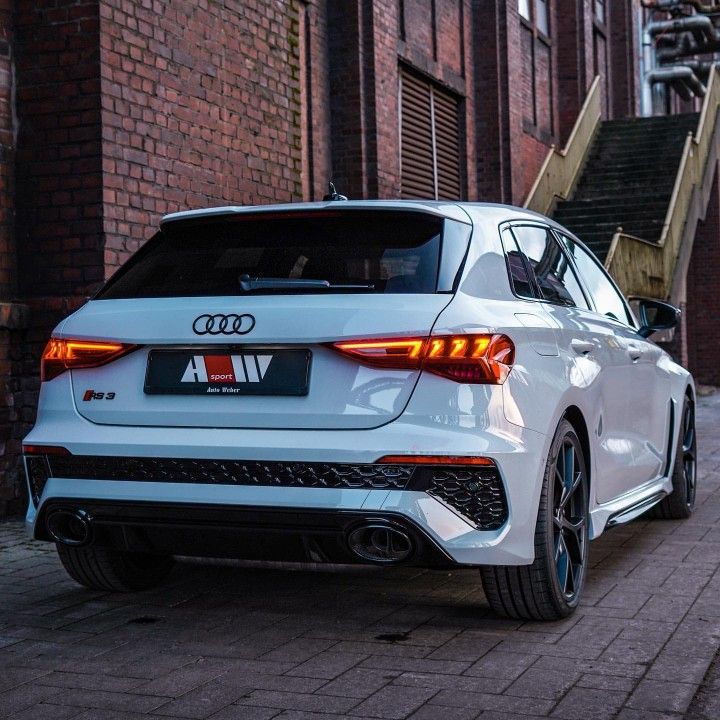 the rear end of a white car parked in front of a brick building