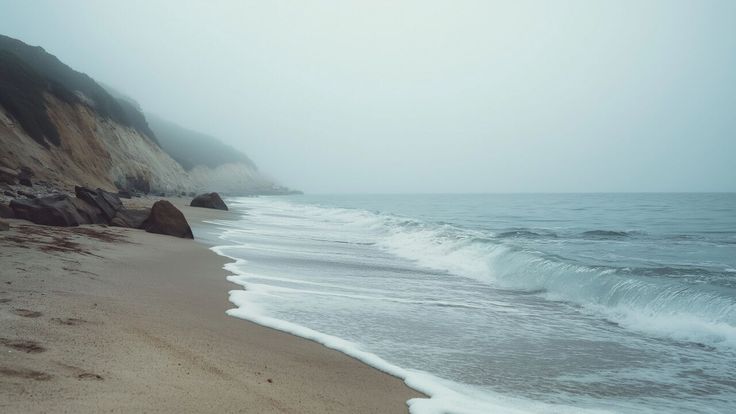 a beach with waves coming in to the shore and cliffs on either side, as seen from the sand