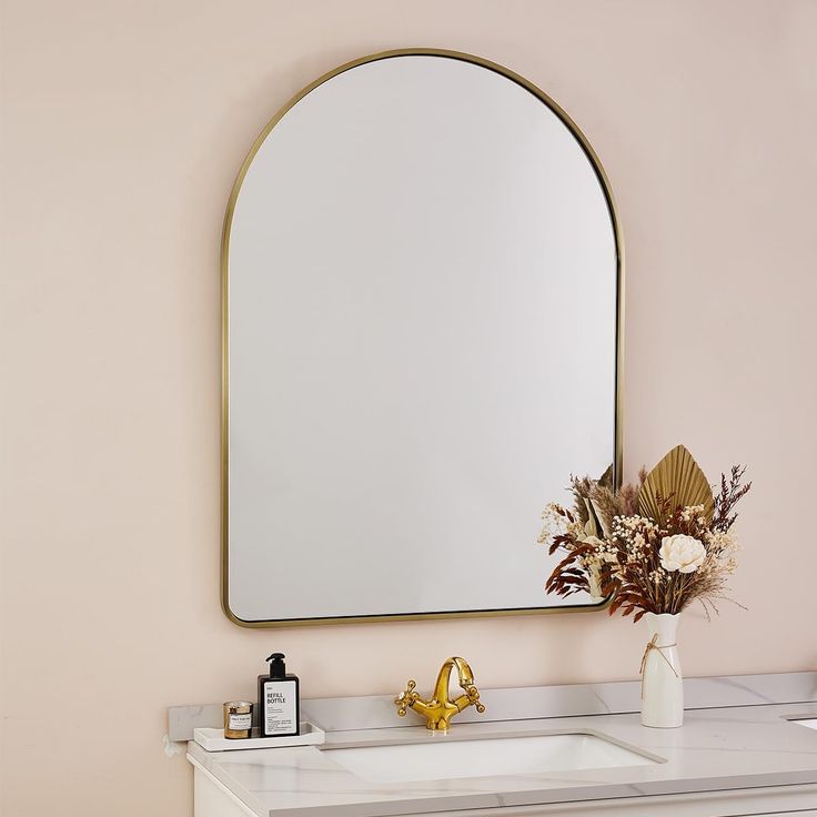 a bathroom vanity with a large mirror above it and flowers in a vase on the counter