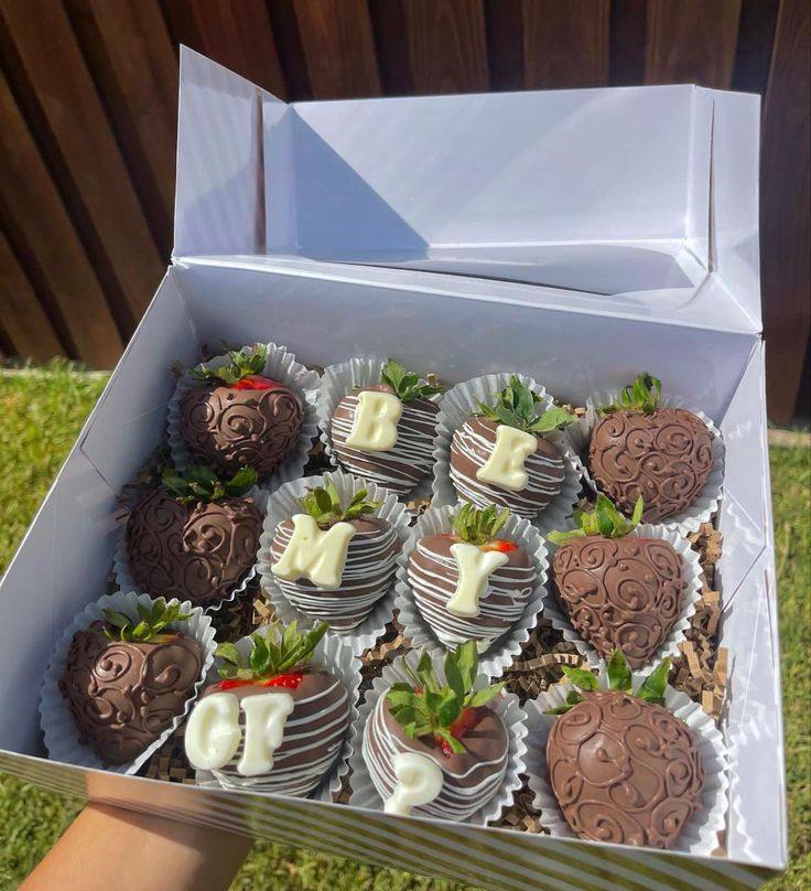 a box filled with chocolate covered strawberries sitting on top of a grass covered field