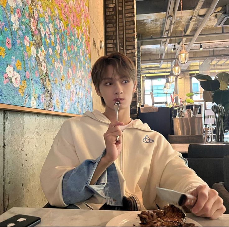 a person sitting at a table with food in front of him and eating from a spoon