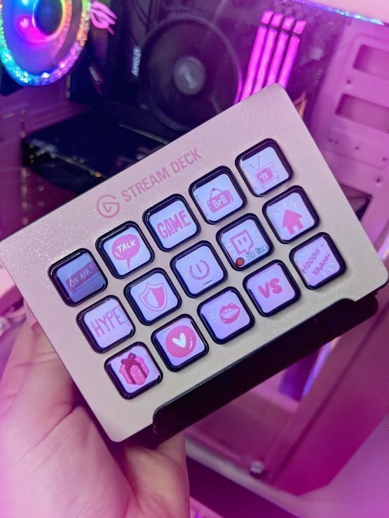 a person holding a pink and black keyboard in front of a computer monitor with neon lights behind it