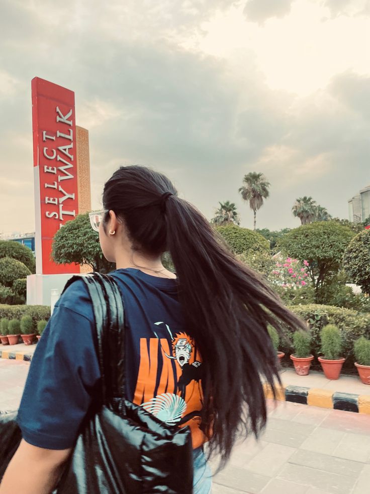 a woman with long black hair walking down the street in front of a store sign