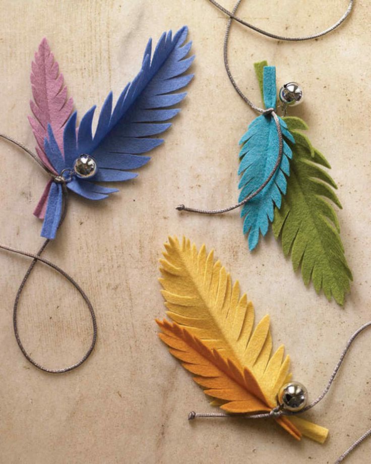 three different colored feathers are hanging from strings on a table, one is silver and the other is yellow