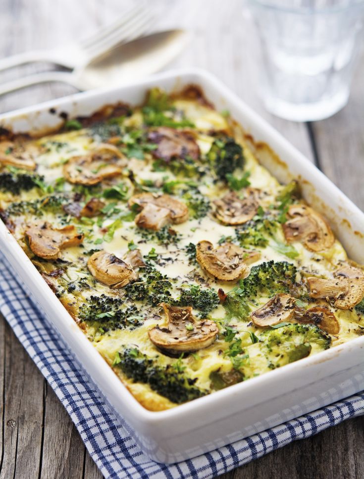 a casserole dish with broccoli, mushrooms and cheese in it on a wooden table