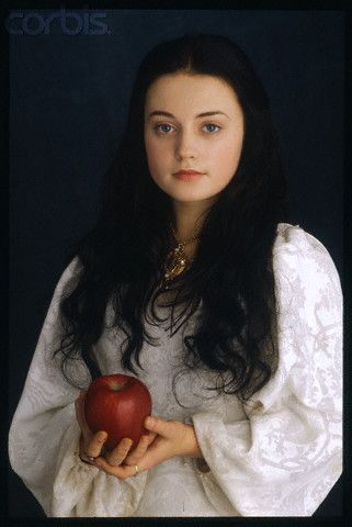 a young woman holding an apple in her right hand and wearing a white cloak over her shoulders