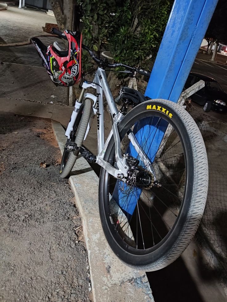 a bicycle parked on the side of a road next to a blue pole and tree