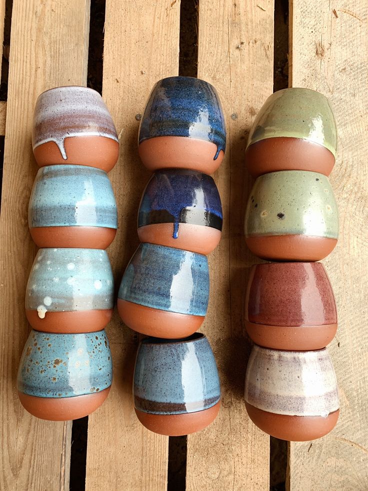 several different colored vases sitting on top of a wooden table next to each other