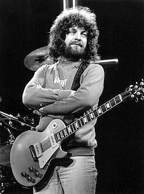 a man with long hair standing next to a guitar