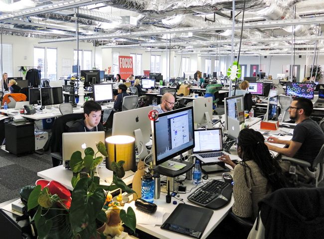 an office filled with lots of computers and people sitting at desks in front of them