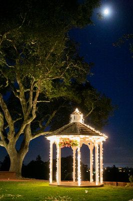 the gazebo is lit up at night with lights on it and trees in the background