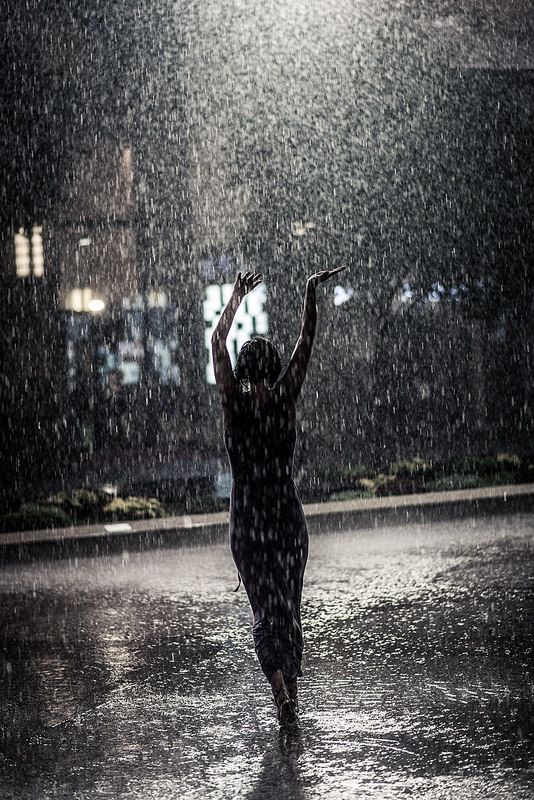 a woman is dancing in the rain with her hands up and an umbrella over her head