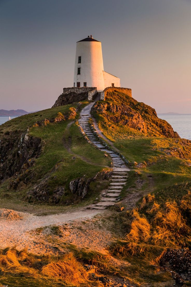 a lighthouse on top of a hill with stairs leading up to the top and water below