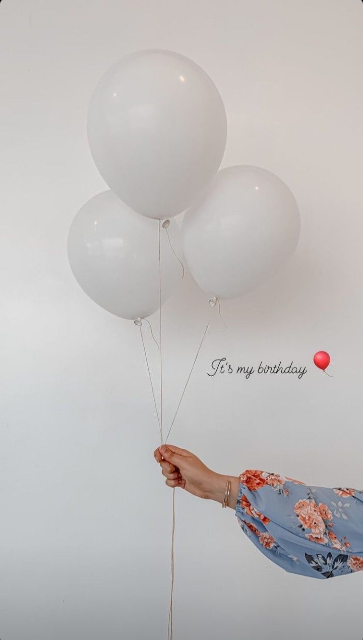 a woman holding three white balloons with the words happy birthday written on one side and an orange balloon in the other