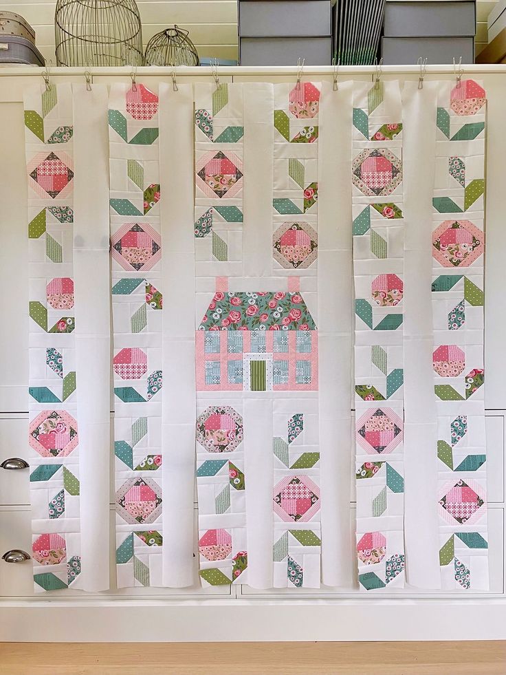 a wall hanging made out of quilts and fabric with pink, green, blue, and white designs on it