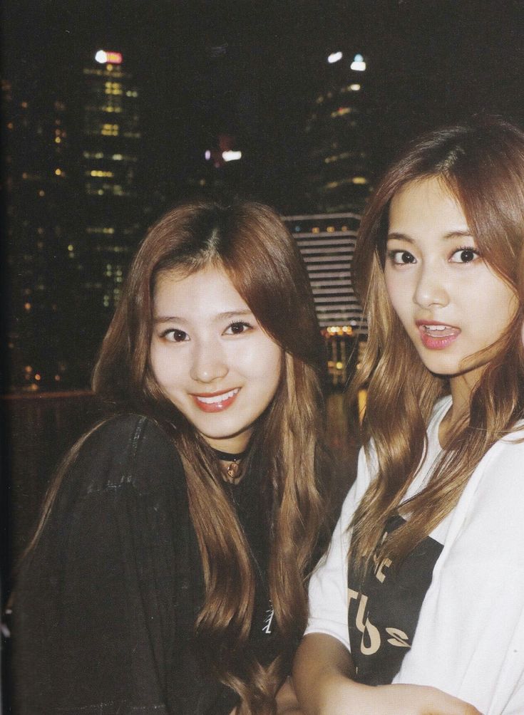 two young women standing next to each other in front of a city skyline at night