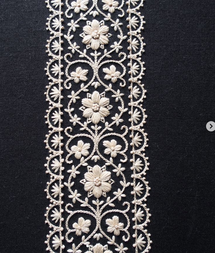 a white lace with flowers and leaves on black fabric, in the shape of a flower