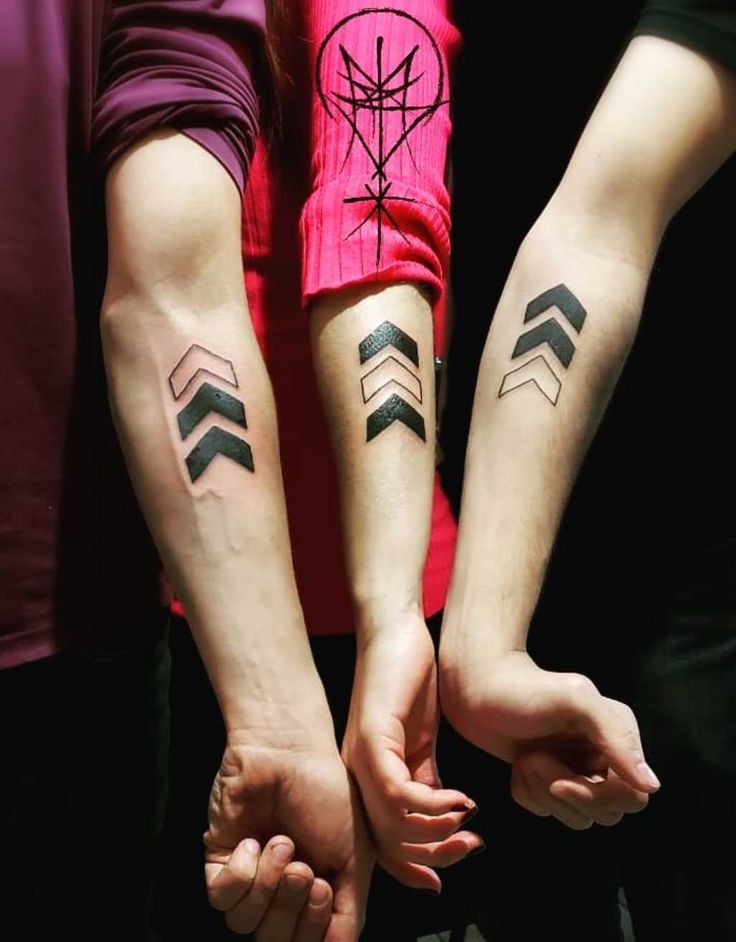 two people holding hands with tattoos on their arms and one has an arrow in the middle