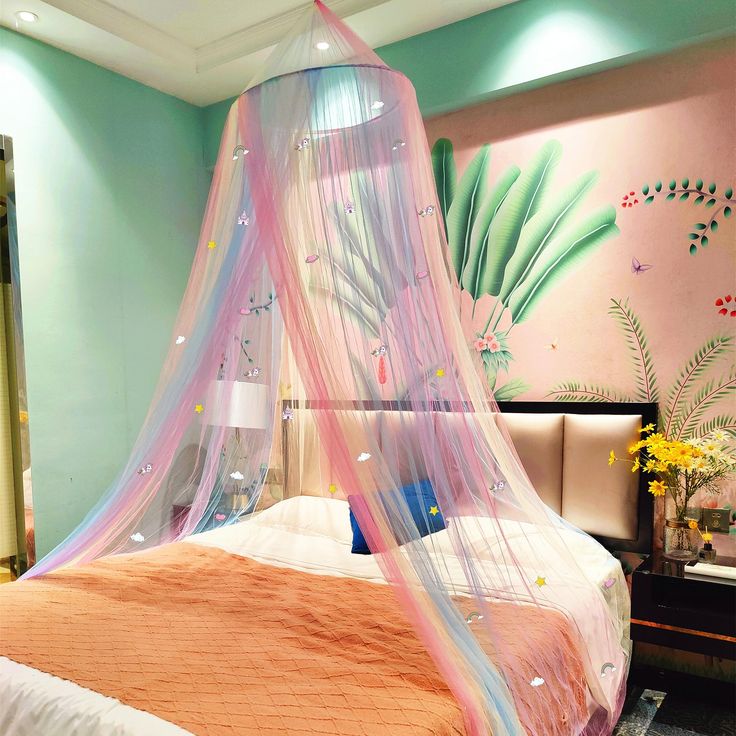 a bed with a pink canopy over it in a room that has flowers on the wall