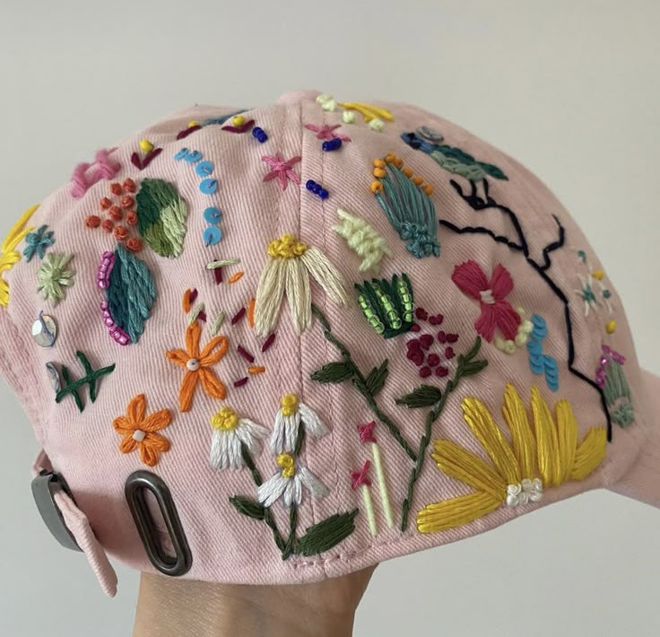 a pink baseball cap with embroidered flowers and leaves on the front, along with an oval metal clip