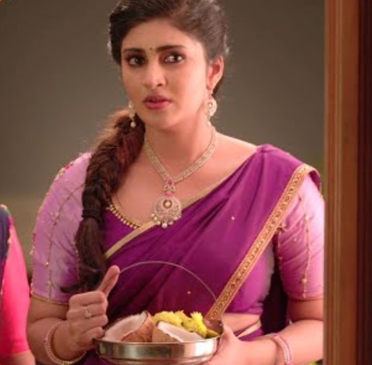 a woman in a sari holding a bowl of food and pointing to the side