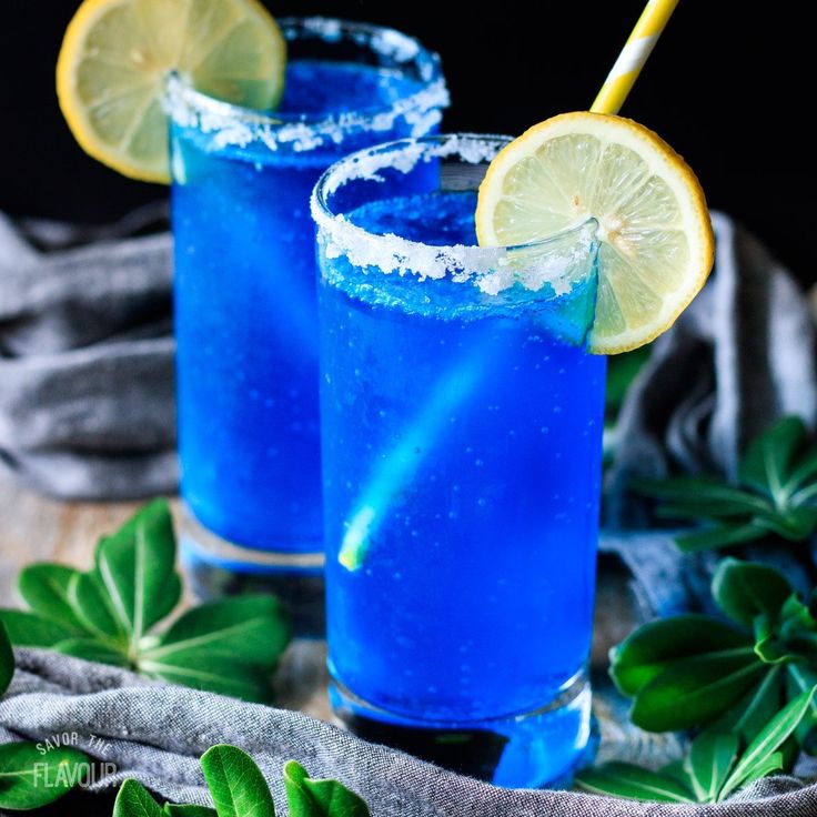 two blue cocktails with lemon wedges and garnishes on the rim