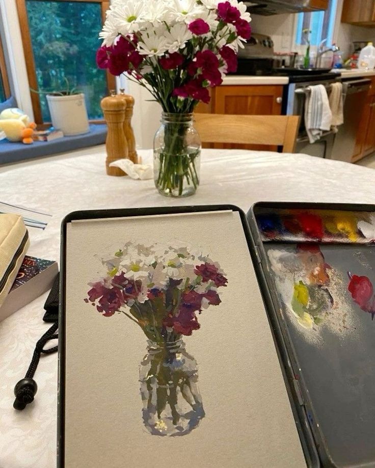 flowers in a vase sitting on top of a table next to an easel with watercolors