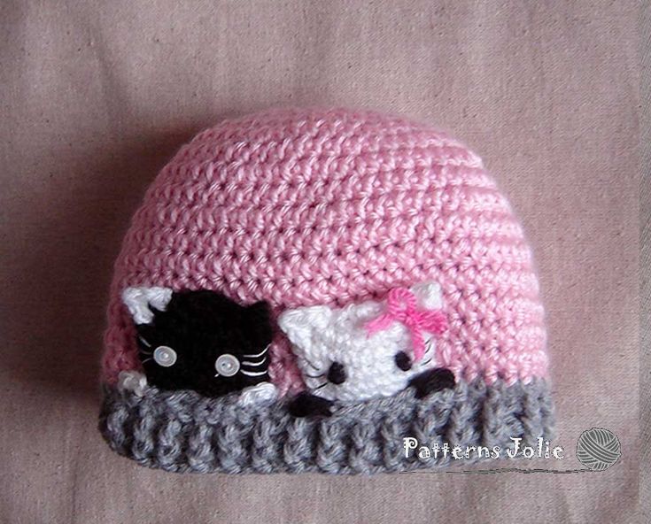 a crocheted hat with two black cats on the front and one white cat on the back