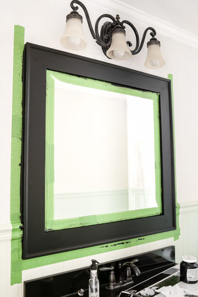 a bathroom mirror that has been painted black and white with green trim around it, along with two lights on either side of the mirror