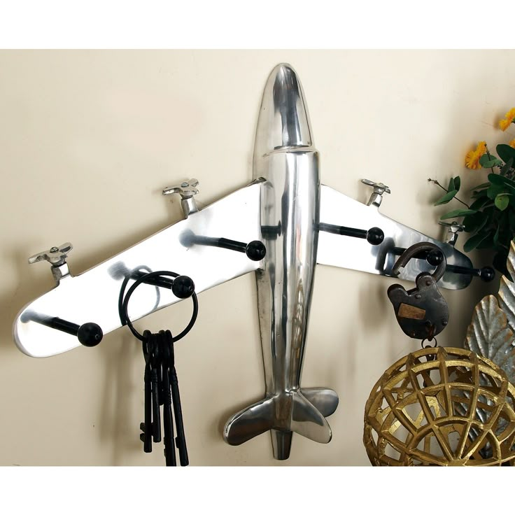 a metal airplane hanging on the wall next to a vase with flowers and other items