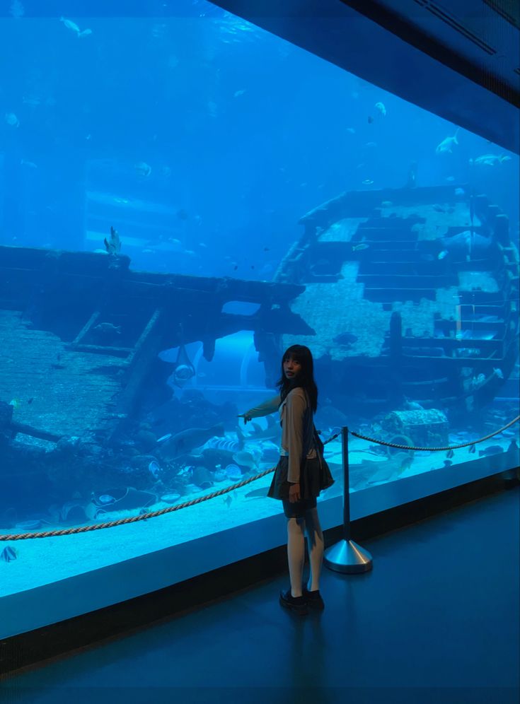 a woman standing in front of an aquarium looking at the water