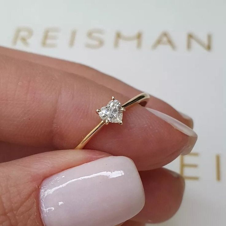 a woman's hand holding a ring with a single diamond on the middle of it