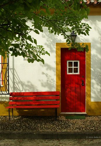 a red door and two benches in front of a white building with yellow trim on it