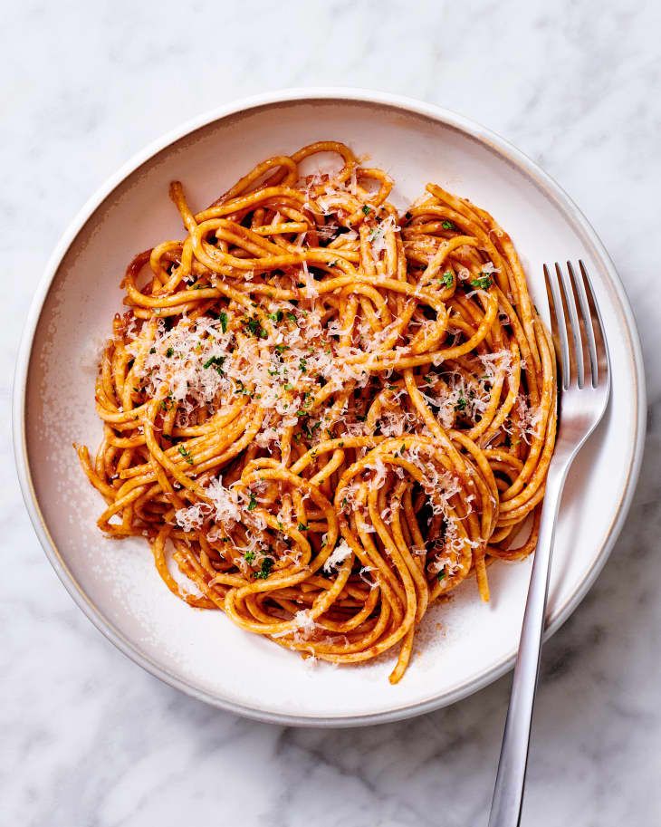 a white bowl filled with spaghetti and topped with parmesan cheese