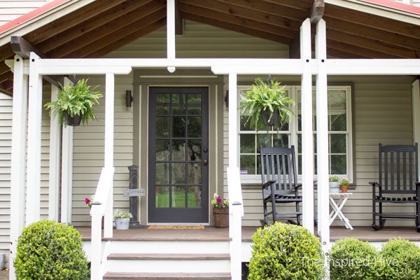 a porch with chairs and potted plants on the front steps, next to a house