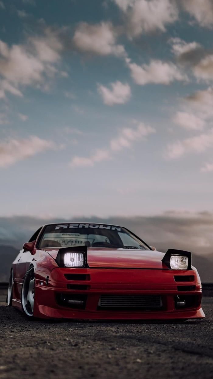 a red sports car parked on the side of a road with clouds in the background