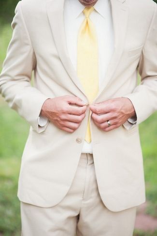 a man wearing a suit and yellow tie with his hands on his chest, standing in the grass