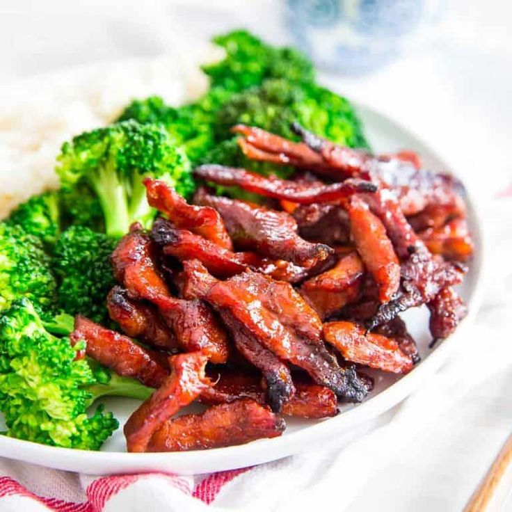 a white plate topped with meat and broccoli on top of a red and white table cloth