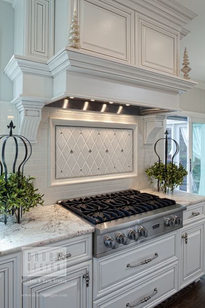 a white kitchen with marble counter tops and stainless steel stove top oven hood in the middle