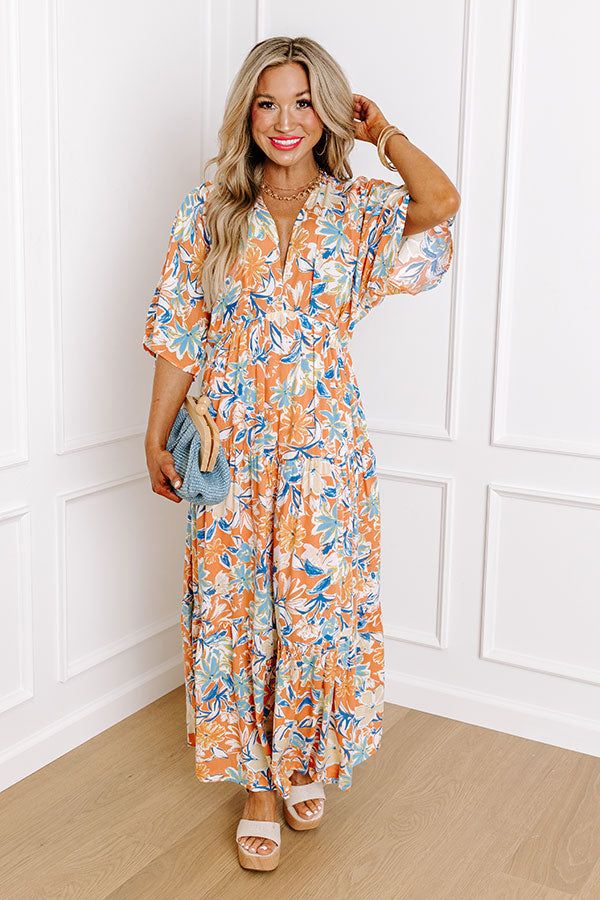 a woman standing in front of a white wall wearing an orange and blue floral print dress