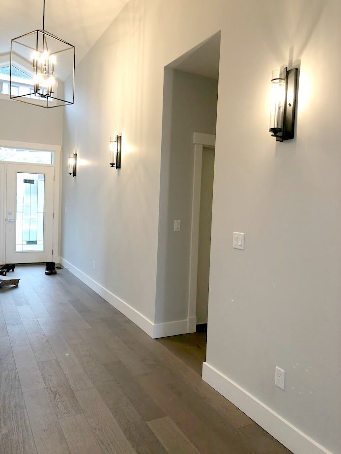 an empty living room with hard wood flooring and white paint on the walls, along with light fixtures