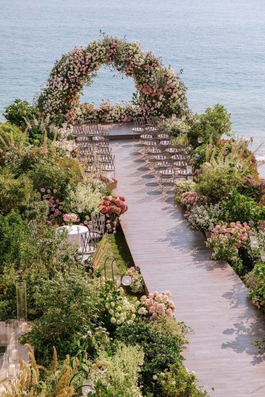 an outdoor ceremony set up with flowers and greenery on the steps leading to the ocean