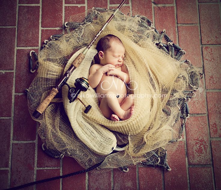 a baby is wrapped in a blanket and holding a fishing rod while sitting on a red brick floor