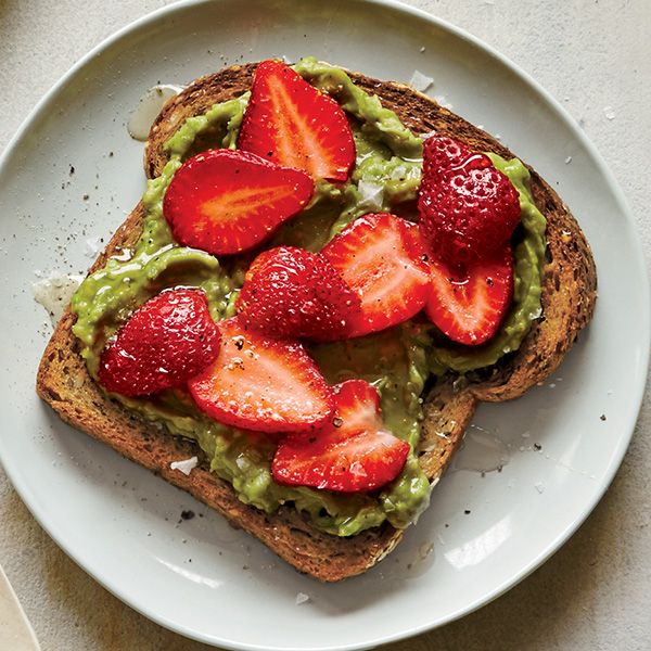 a white plate topped with toast covered in guacamole and strawberries