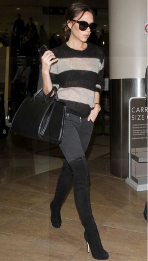 a woman walking through an airport carrying a black purse and wearing high heeled boots