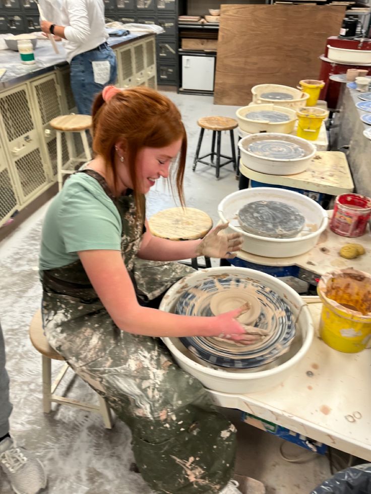 a woman sitting at a table making pottery