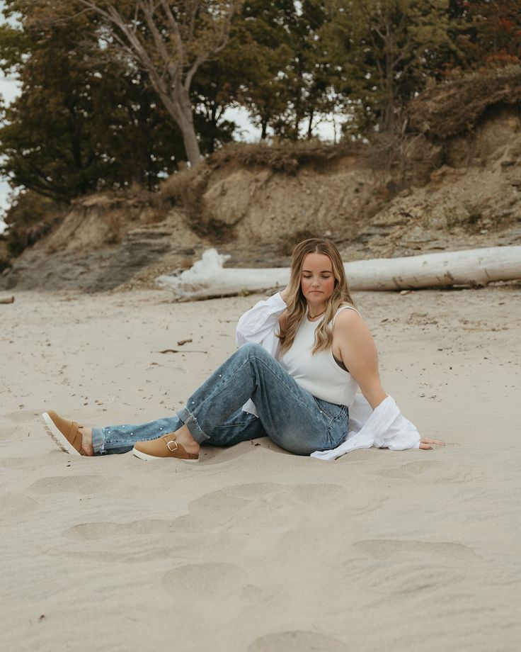 a woman sitting in the sand with her legs crossed