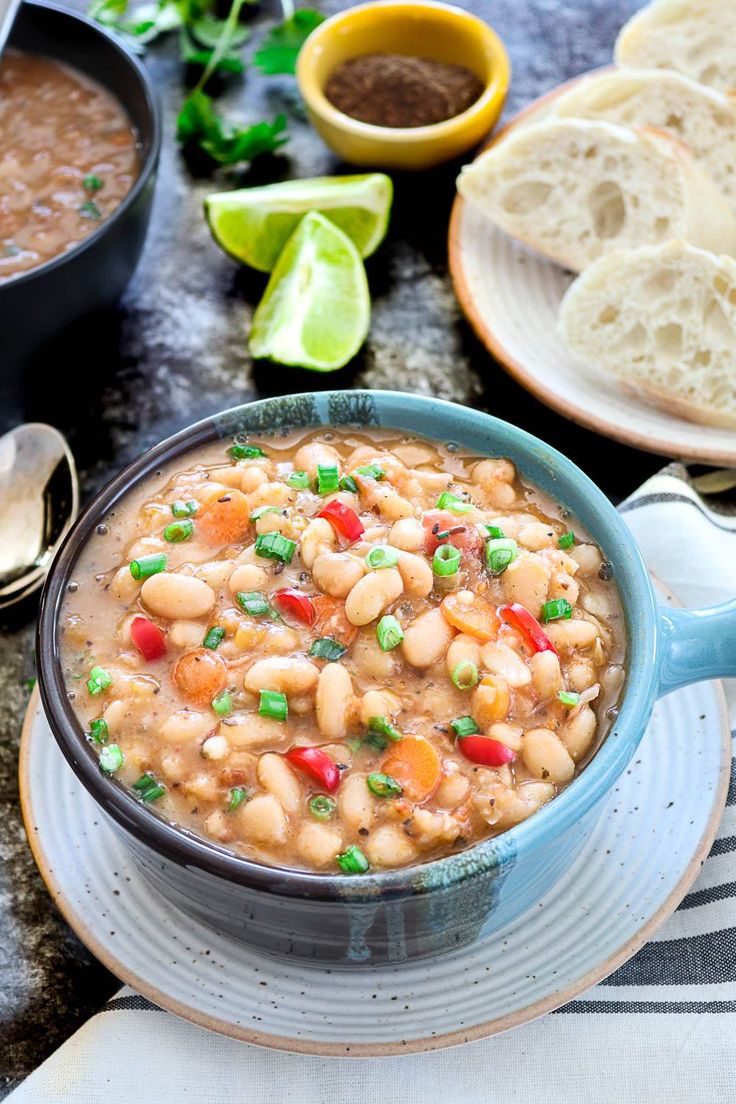 a bowl filled with beans and vegetables on top of a white plate next to bread